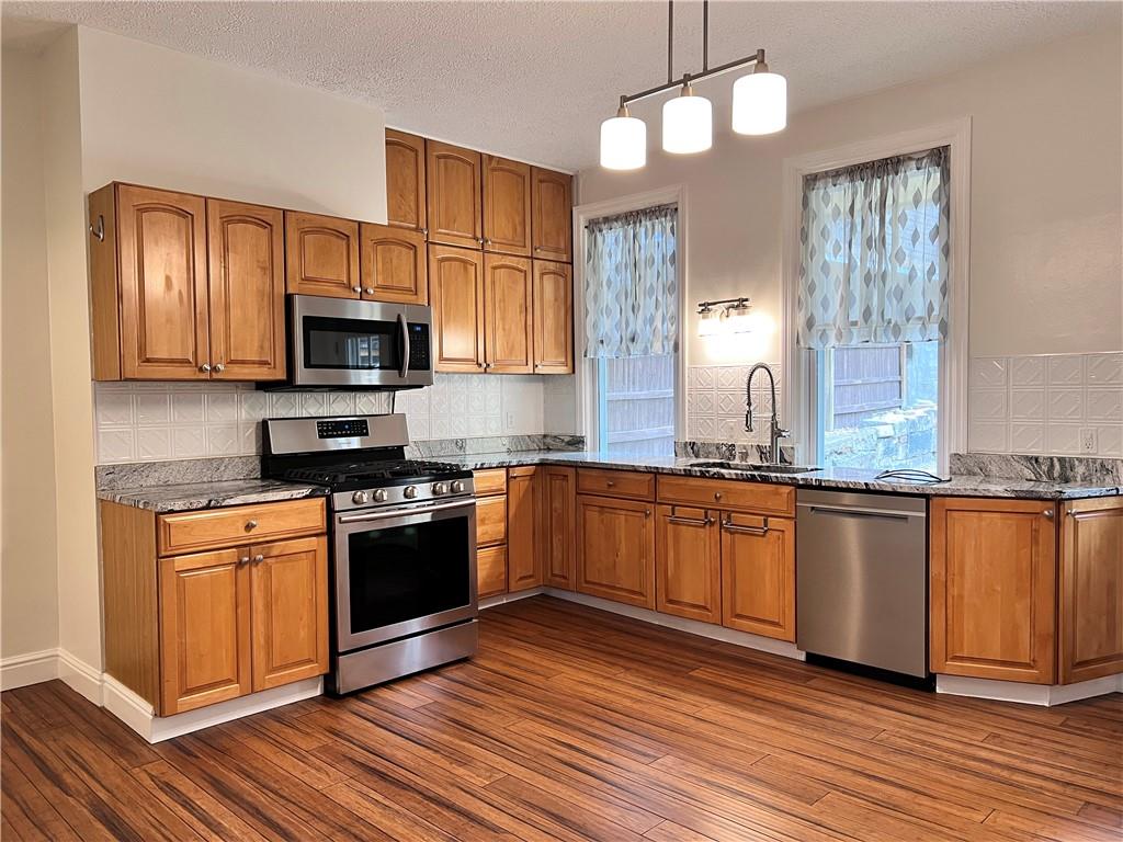 5266 Natrona Way Pittsburgh, PA 15201 - Photo 5 of 13 a kitchen with stainless steel appliances granite countertop a sink a stove a microwave oven a refrigerator with wooden floor and cabinets