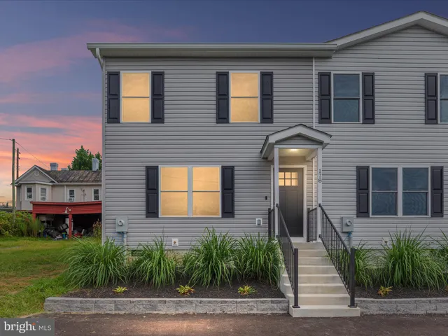 a view of a brick house with a yard plants and large tree