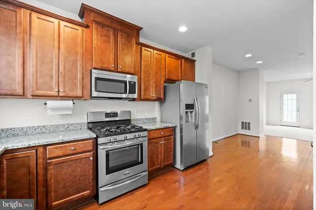 a kitchen with stainless steel appliances granite countertop a refrigerator stove top oven and sink with wooden floor