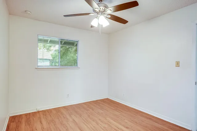 an empty room with wooden floor chandelier fan and windows