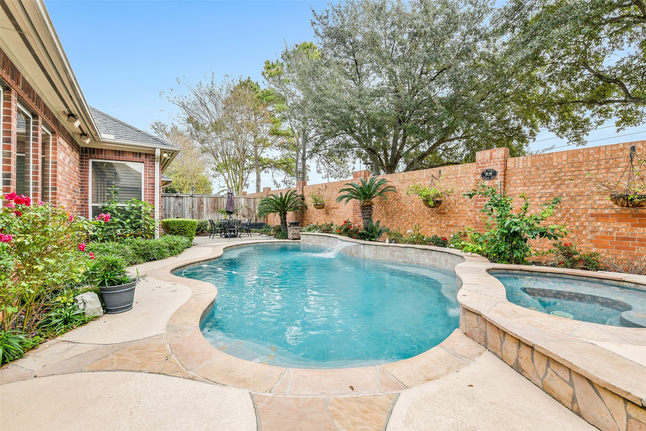 11413 Gallant Ridge Lane Houston, TX 77082 - Photo 2 of 50 sparkling pool surrounded by lush greenery and privacy-enhancing brick walls. A stylish patio area with wrought-iron furniture and a large umbrella provides a perfect spot for outdoor dining and relaxation.