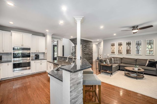 a kitchen with stainless steel appliances granite countertop a stove and a view of living room with furniture