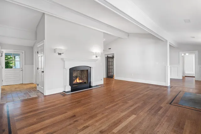 a view of an empty room with wooden floor fireplace and a window