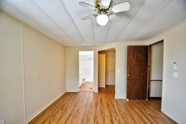 a view of an empty room with chandelier fan and wooden floor