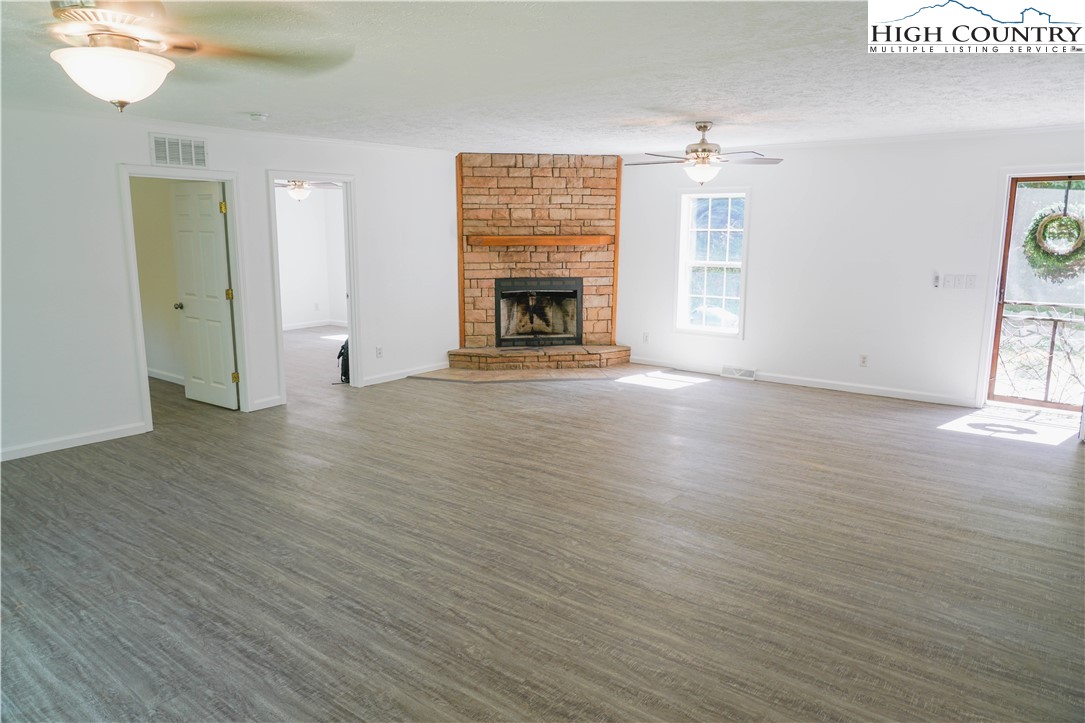 3906 Junaluska Road Boone, NC 28607 - Photo 12 of 39 an empty room with wooden floor a fireplace and windows