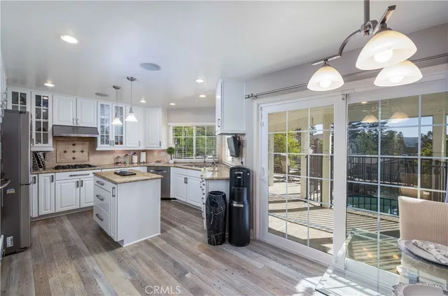 a kitchen with stainless steel appliances granite countertop a stove a refrigerator a sink a dining table and chairs with wooden floor