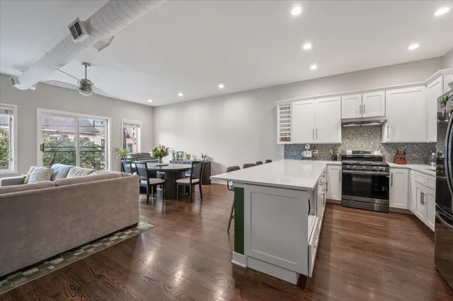 a living room with stainless steel appliances furniture wooden floor and a kitchen view