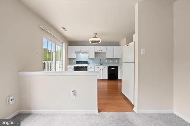 a large white kitchen with kitchen island a stove a refrigerator a sink dishwasher and white cabinets with wooden floor