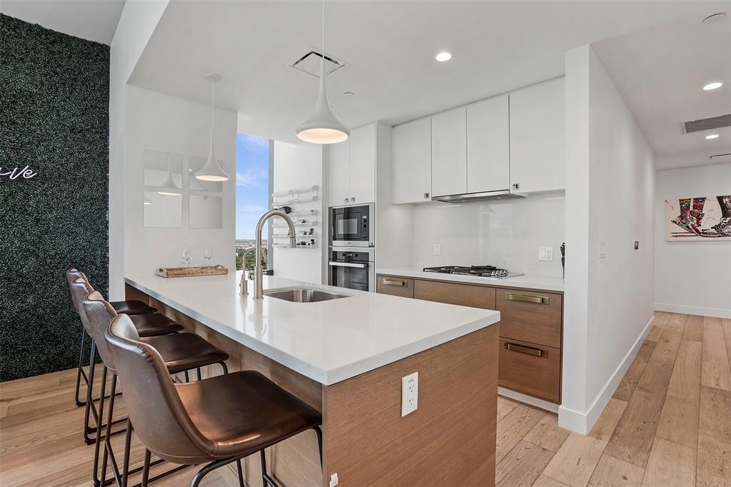 70 Rainey Street, Unit 1409 Austin, TX 78701 - Photo 5 of 38 Dual tone kitchen with two tone cabinets, light wood-type flooring, hanging light fixtures, a kitchen breakfast bar, and stainless steel appliances
