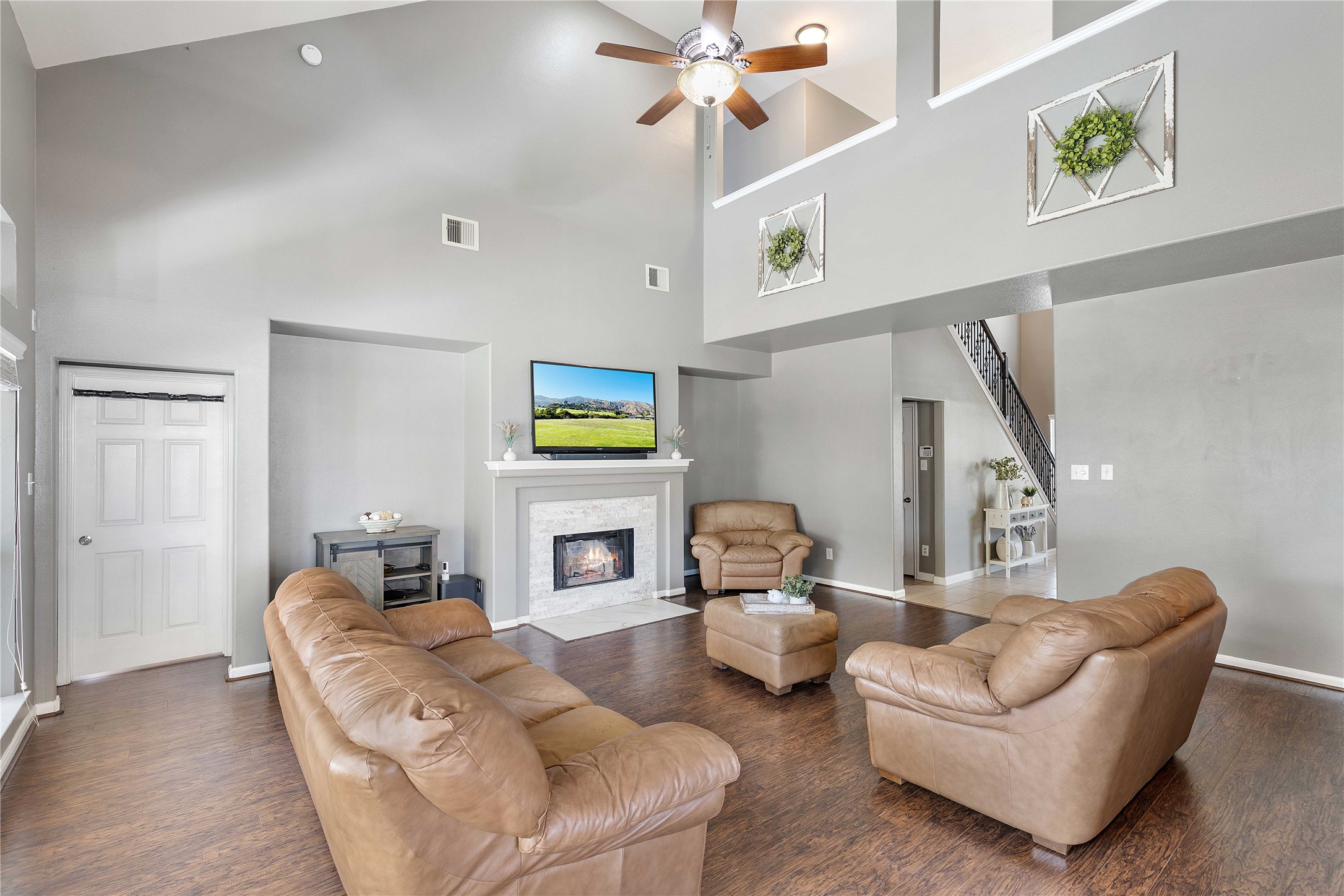 24506 Fort Path Drive Spring, TX 77373 - Photo 8 of 46 Spacious living room with high ceilings, featuring a cozy fireplace, elegant wood plank flooring, and comfortable leather seating.