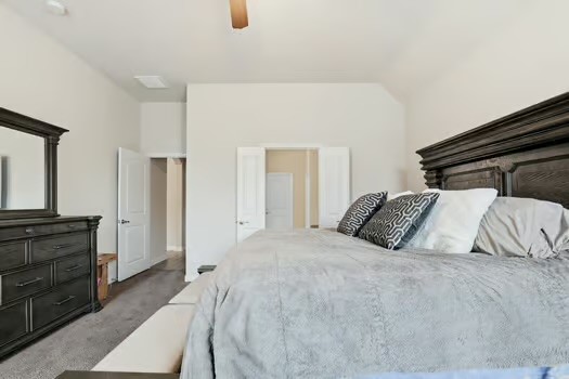 24714 Longwood Forest Drive Spring, TX 77373 - Photo 11 of 21 Spacious bedroom with neutral colors, featuring a large bed with decorative pillows, a dark wood dresser with a mirror, and a carpeted floor. There's ample natural light and an open doorway leading to additional space.