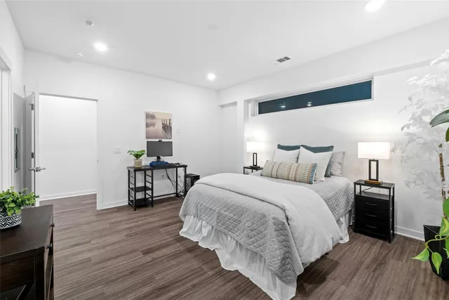 a spacious bedroom with a bed a dresser and wooden floor