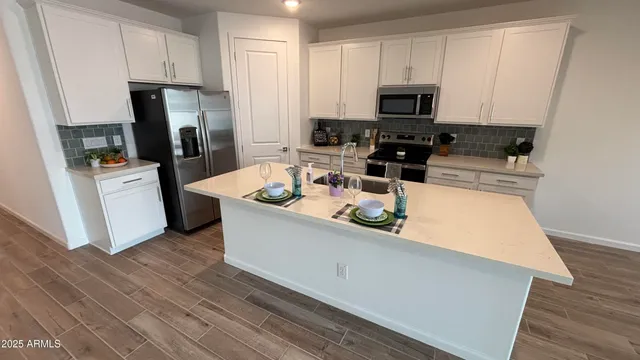 a kitchen with stainless steel appliances a stove a refrigerator a sink a stove and white cabinets with wooden floor