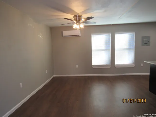 an empty room with wooden floor fan and windows