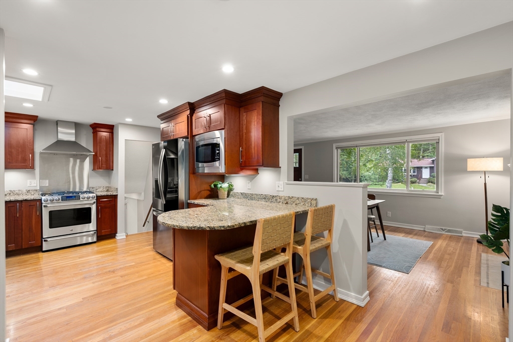 73 Willow Road Sudbury, MA 01776 - Photo 14 of 41 a kitchen with stainless steel appliances kitchen island granite countertop a stove a refrigerator a sink a dining table and chairs with wooden floor