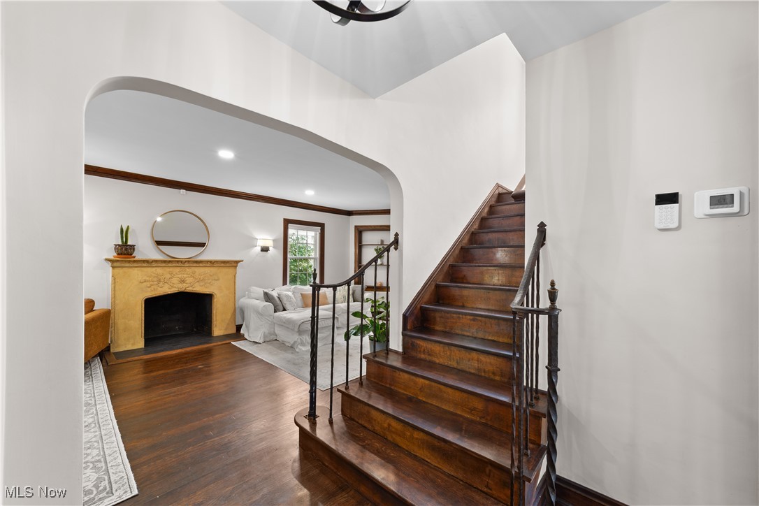 Stairs featuring arched walkways, wood finished floors, crown molding, a fireplace with flush hearth, and recessed lighting
