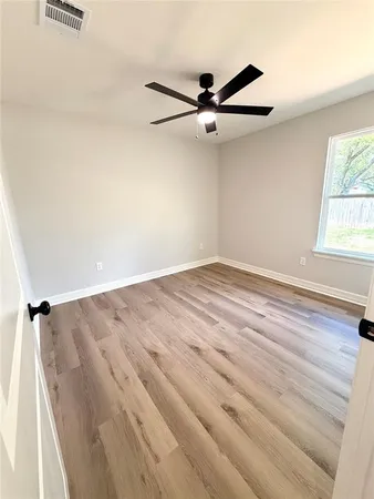 an empty room with wooden floor fan and windows