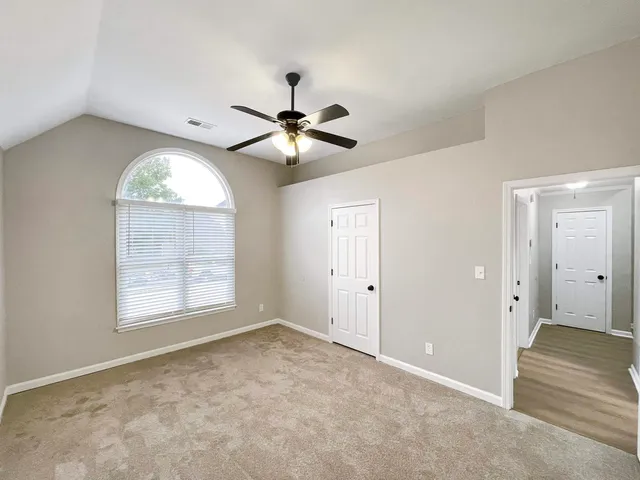 an empty room with chandelier fan and windows