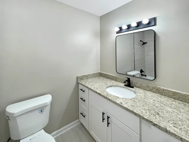 a bathroom with a granite countertop sink a toilet and mirror