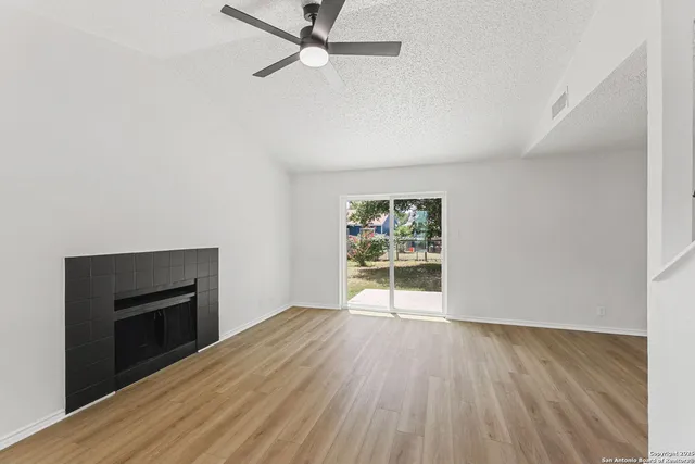 an empty room with wooden floor fireplace and windows