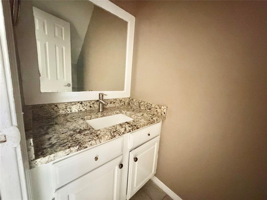 8001 Rothington Road, Unit 33 Dallas, TX 75227 - Photo 14 of 15 Vanity featuring a white cabinet base with gold-toned hardware, an undermount sink, a patterned stone countertop, and a brushed nickel faucet