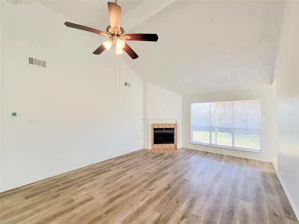 a view of an empty room with chandelier fan and fire place