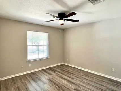 an empty room with wooden floor ceiling fan and windows