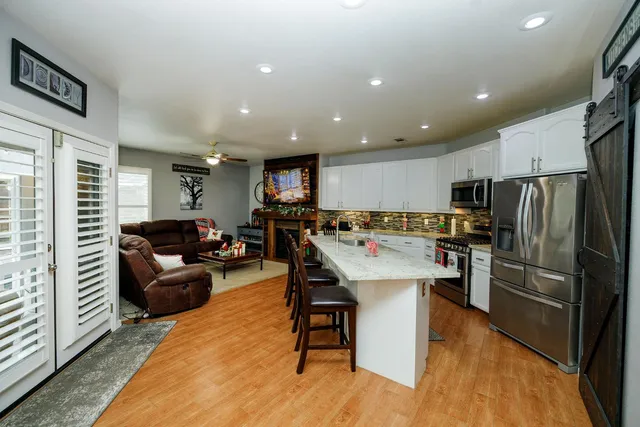 a kitchen with stainless steel appliances kitchen island granite countertop a refrigerator a stove a sink a dining table and chairs with wooden floor