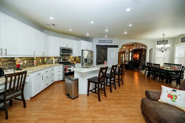 a kitchen with stainless steel appliances kitchen island granite countertop a refrigerator a stove a sink a dining table and chairs with wooden floor