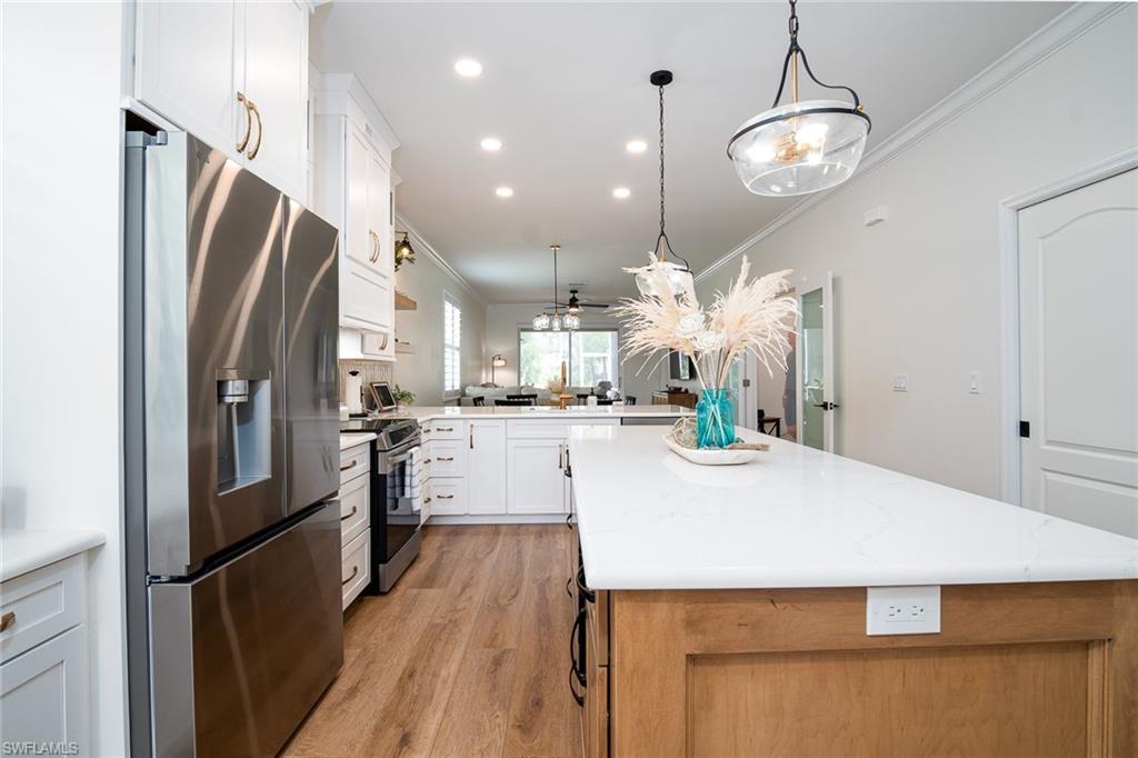 21441 Knighton Run Estero, FL 33928 - Photo 9 of 50 a kitchen with stainless steel appliances a refrigerator a stove a sink and a dining table with wooden floor