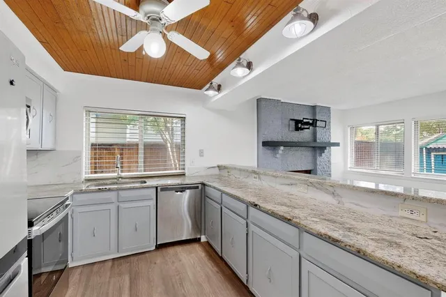 a kitchen with a sink dishwasher a stove and white cabinets with wooden floor