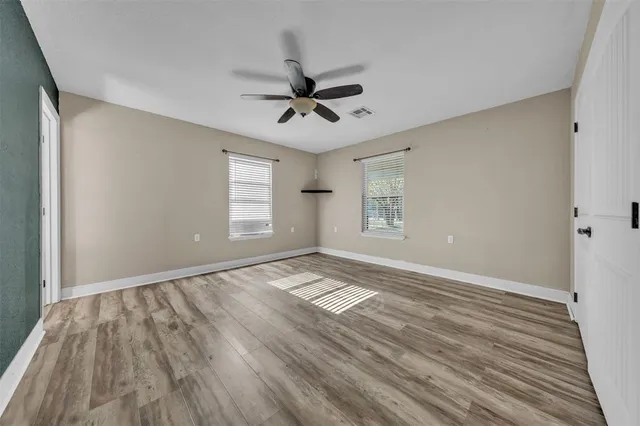 an empty room with wooden floor and a ceiling fan