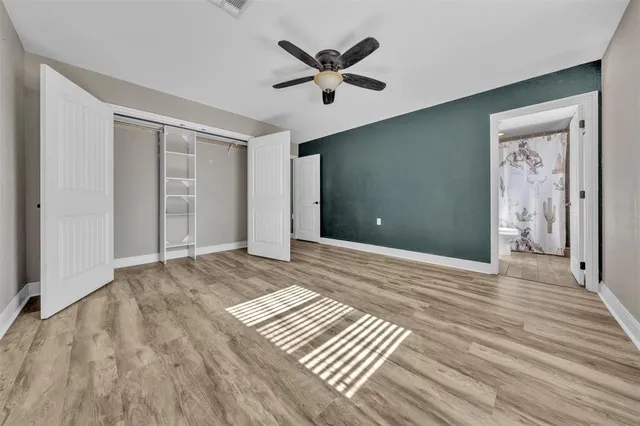a view of an empty room with wooden floor and a ceiling fan