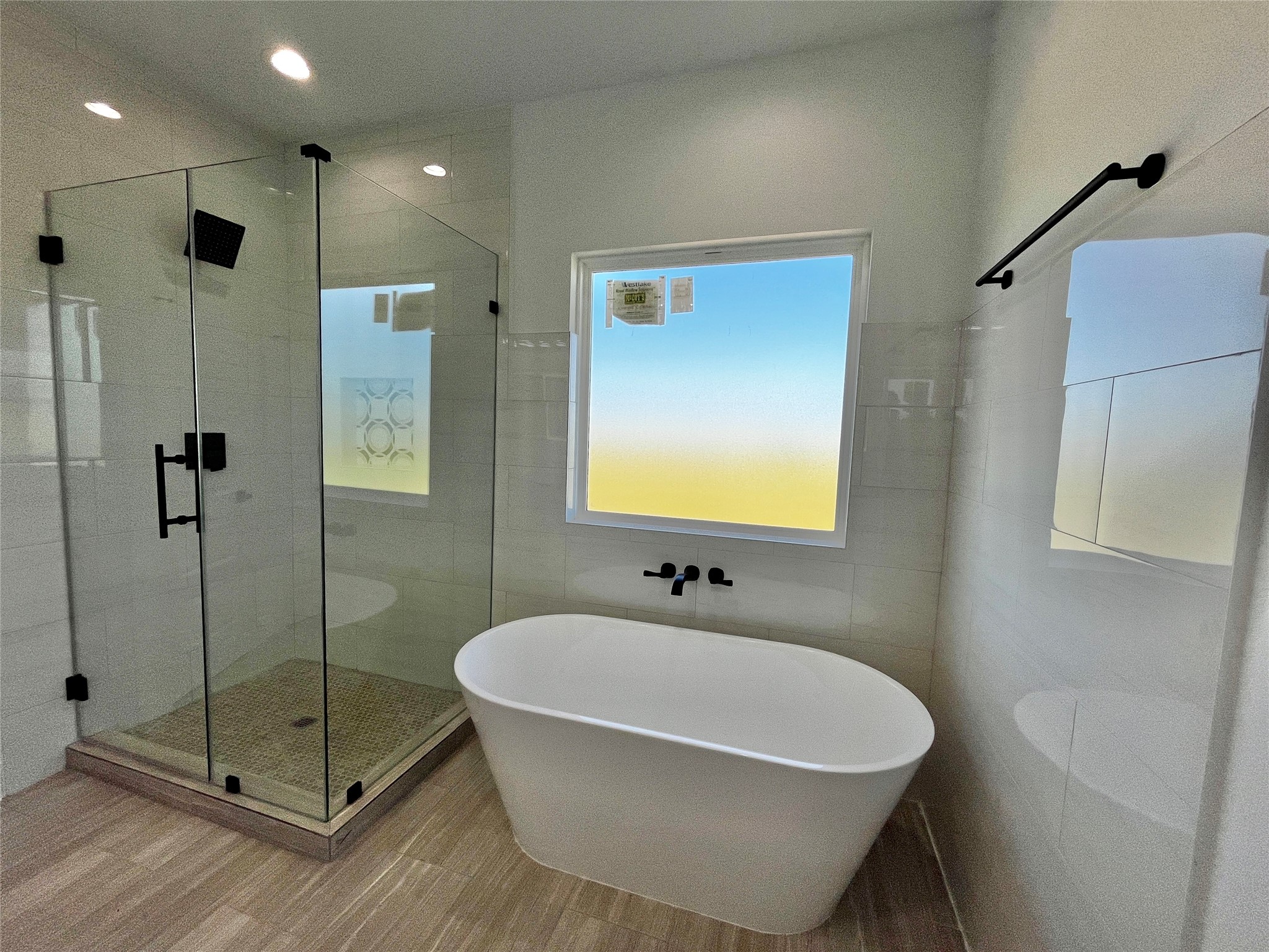 471 Buffalo Trail Angleton, TX 77515 - Photo 27 of 35 This bathroom features a modern design with a sleek freestanding tub, a spacious glass-enclosed shower, and stylish black fixtures. Natural light fills the space through a large window, complementing the neutral tile flooring and walls.
