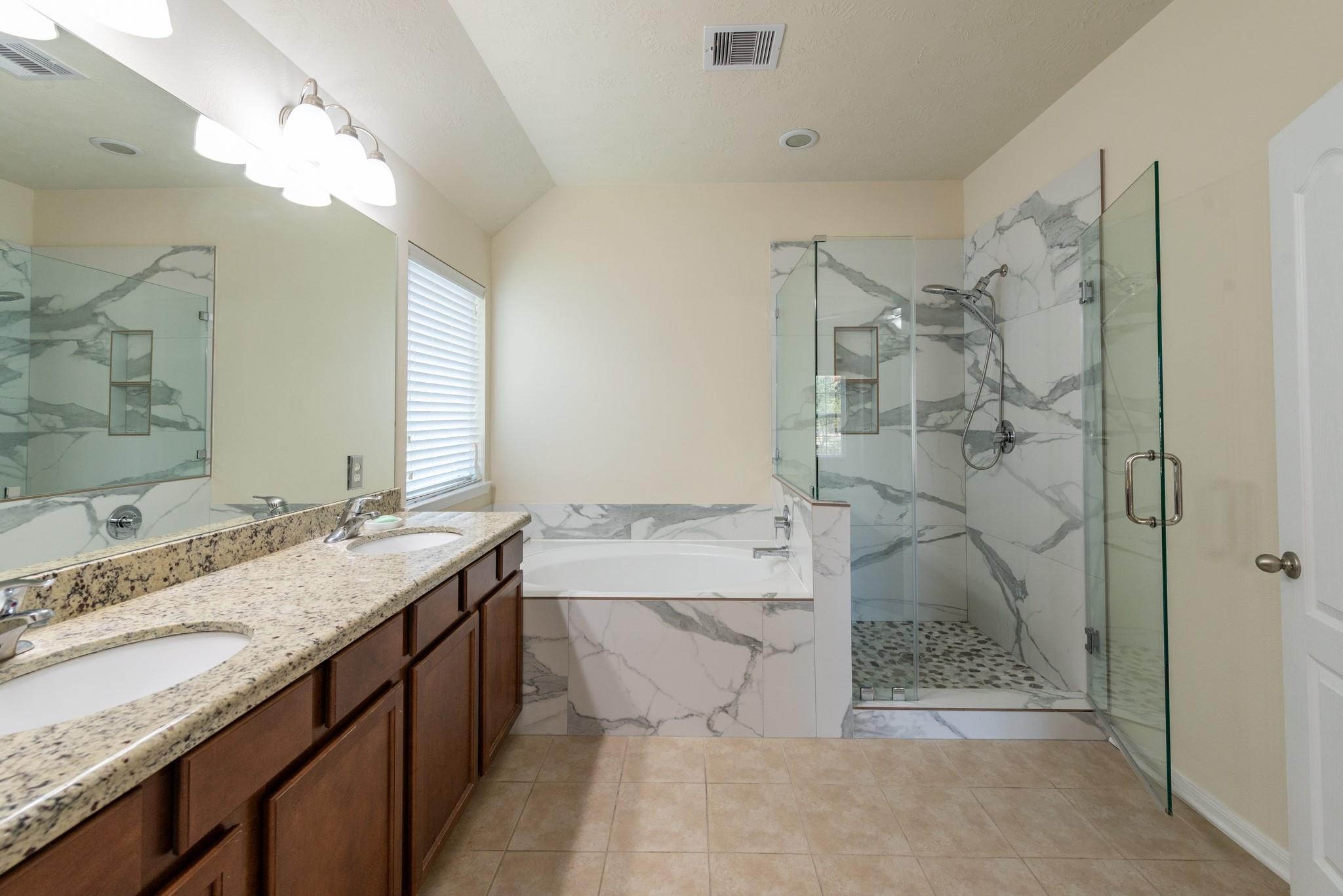6402 Addlestone Ridge Lane Katy, TX 77494 - Photo 14 of 25 Luxurious primary en-suite bathroom featuring dual granite vanities, a soaking tub, and a beautifully updated frameless glass shower with designer tile surround and pebble-stone flooring. This spa-inspired retreat offers the perfect place to start and end your day.