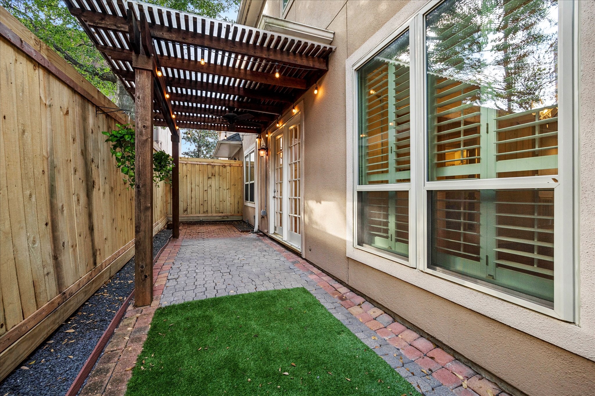 5823 Augusta Court Houston, TX 77057 - Photo 44 of 44 A private and cozy outdoor patio area with a wooden pergola, brick and stone paving, and a section of artificial grass. The space is enclosed by a wooden fence and features large windows with shutters, offering a blend of privacy and natural light. Perfect for relaxation or entertaining.