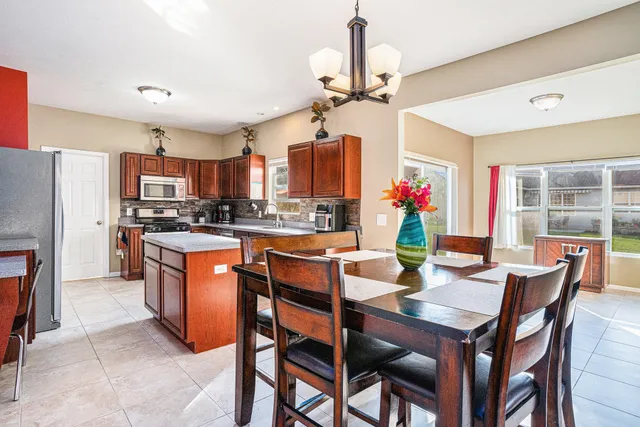 a dining room with stainless steel appliances kitchen island granite countertop a dining table chairs and a refrigerator