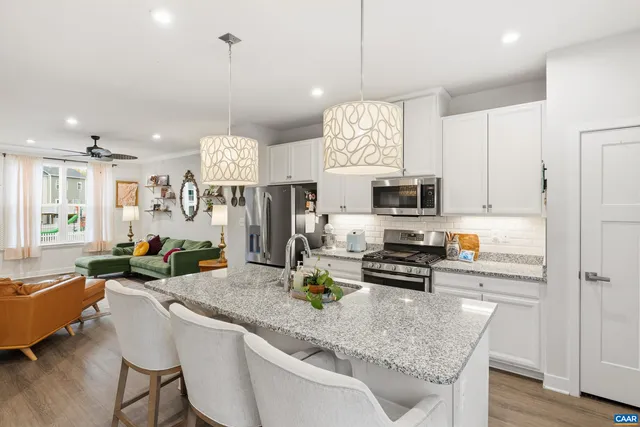 a kitchen with stainless steel appliances granite countertop a stove top oven a refrigerator a sink and white cabinets with wooden floor