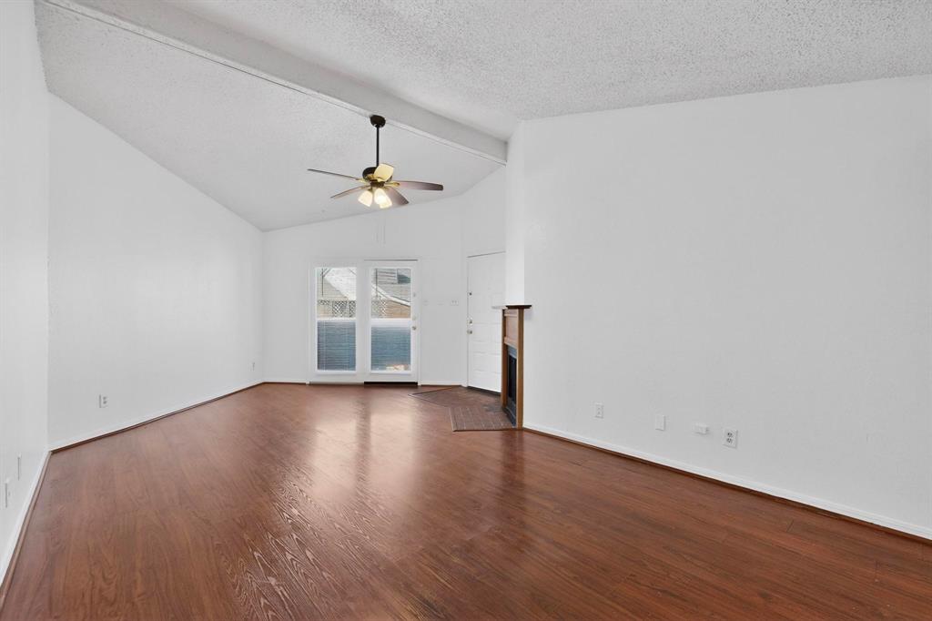 8545 Midpark Road, Unit 16 Dallas, TX 75240 - Photo 3 of 29 Unfurnished living room featuring a brick fireplace, dark wood finished floors, a ceiling fan, and beam ceiling