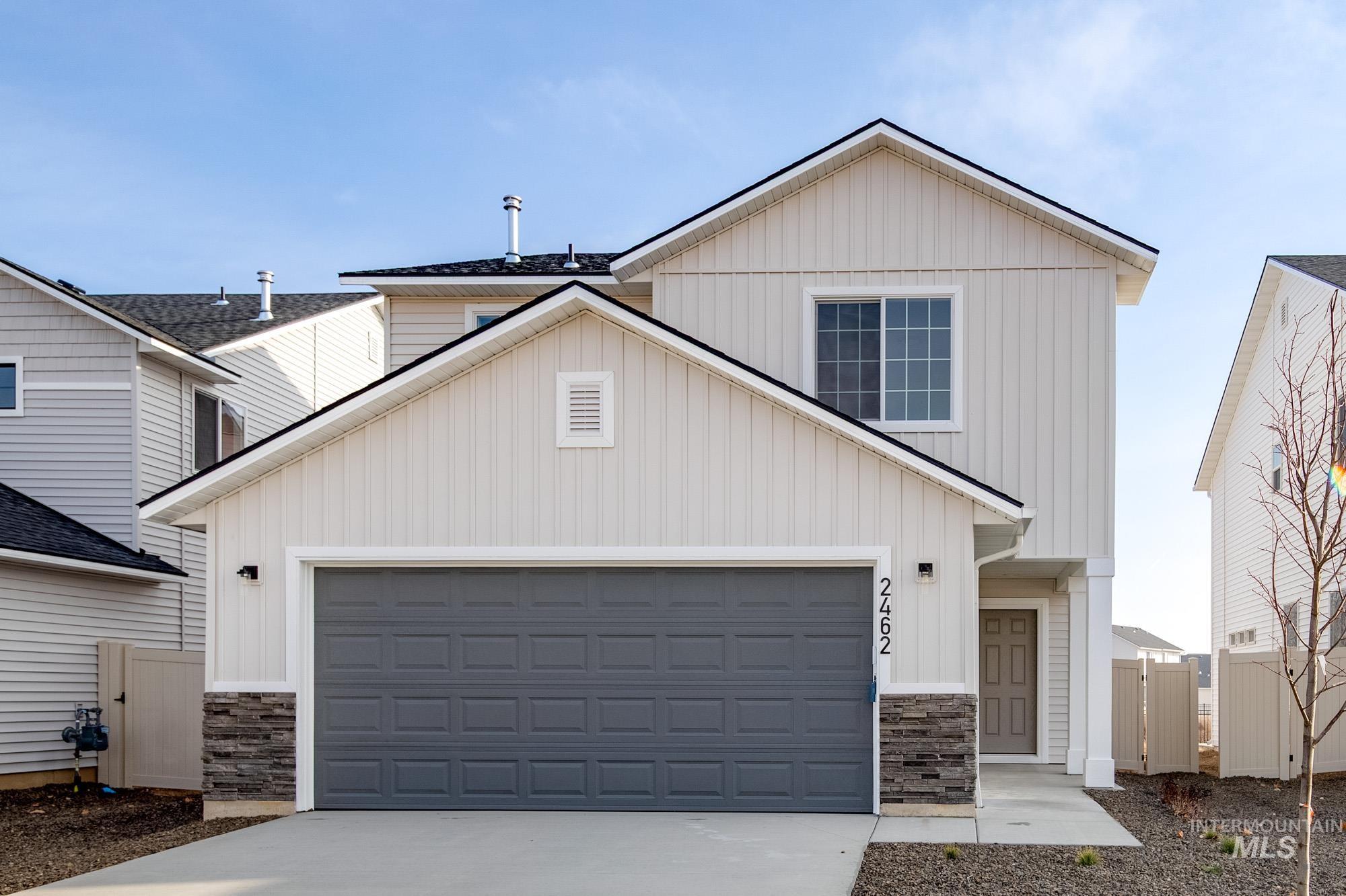 View of front facade featuring board and batten siding, concrete driveway, a gate, and stone siding