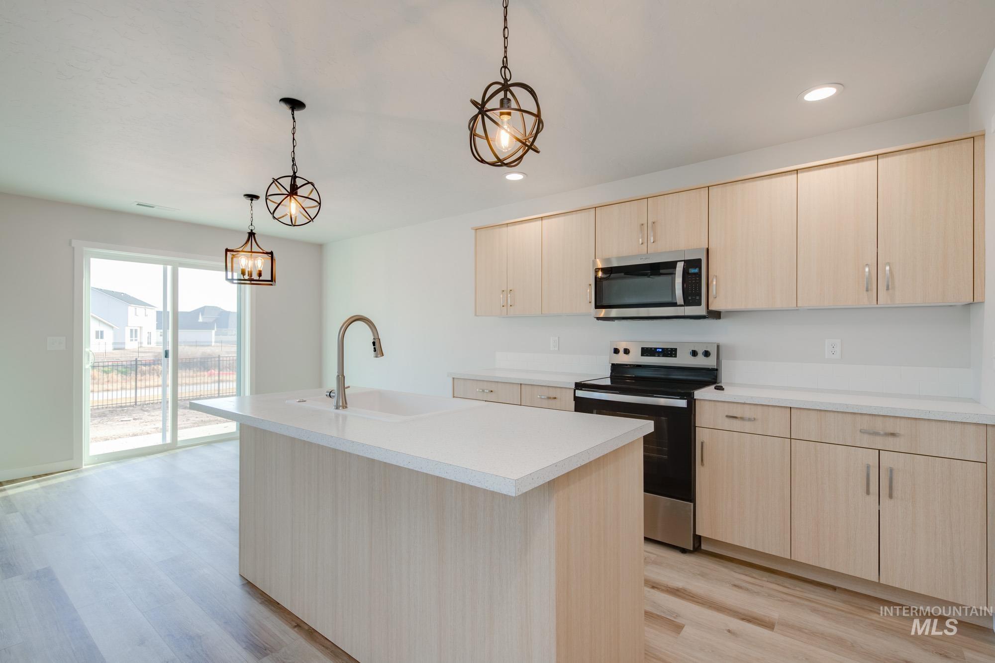 2462 West Fallon Loop Nampa, ID 83651 - Photo 4 of 23 Kitchen featuring stainless steel appliances, light brown cabinets, an island with sink, light countertops, and pendant lighting