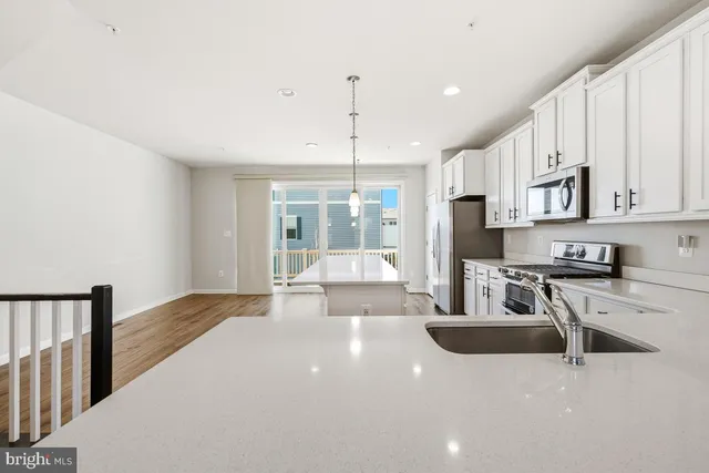 a kitchen with stainless steel appliances granite countertop a stove a sink dishwasher a refrigerator and white cabinets with wooden floor