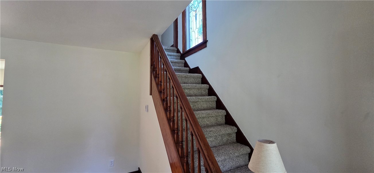9964 East River Road Elyria, OH 44035 - Photo 8 of 45 Staircase featuring wood-finish banister and newel posts, carpeted treads, and a stained-glass window at the landing