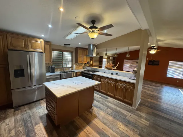 a kitchen with stainless steel appliances granite countertop a refrigerator a sink dishwasher and a stove with wooden floor