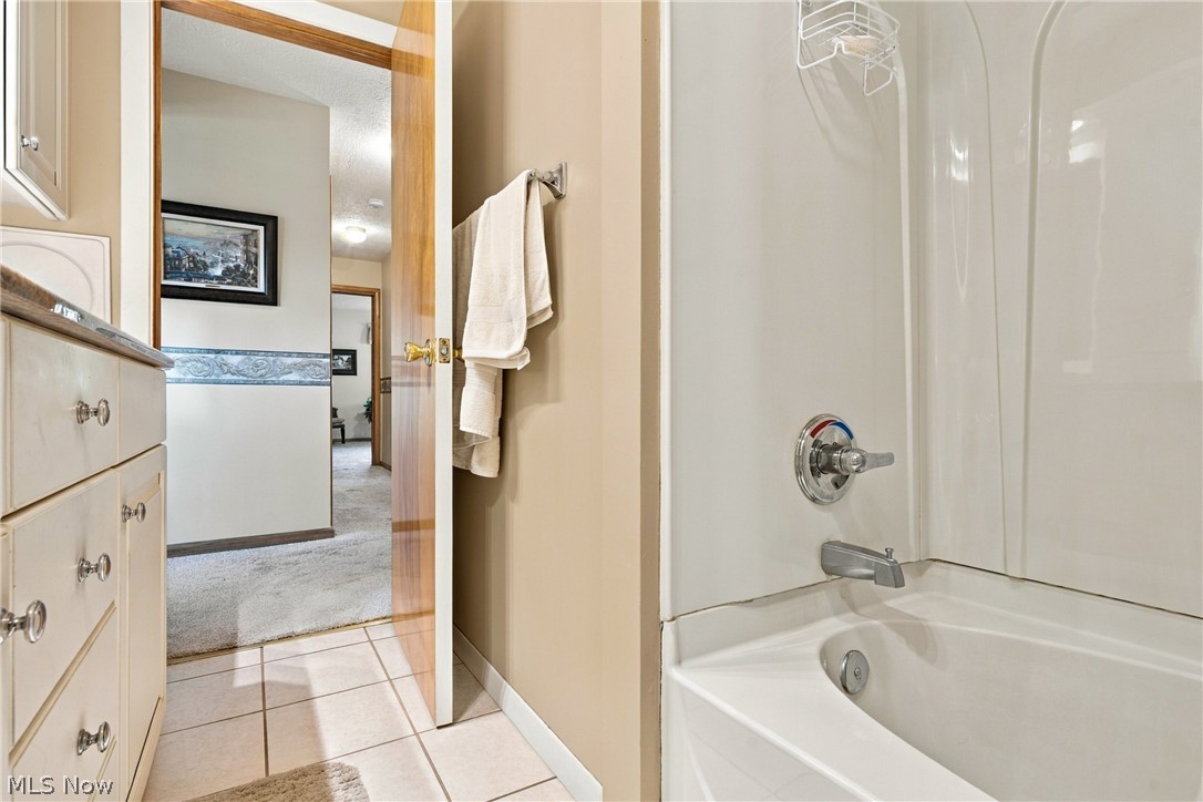 1211 Etter Road Mogadore, OH 44260 - Photo 31 of 48 White bathtub and shower combination with a chrome faucet, light-toned wall paint, white tile flooring, and a vanity with cabinet storage