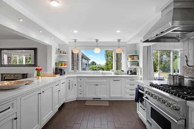 a large white kitchen with stainless steel appliances granite countertop a stove and a sink