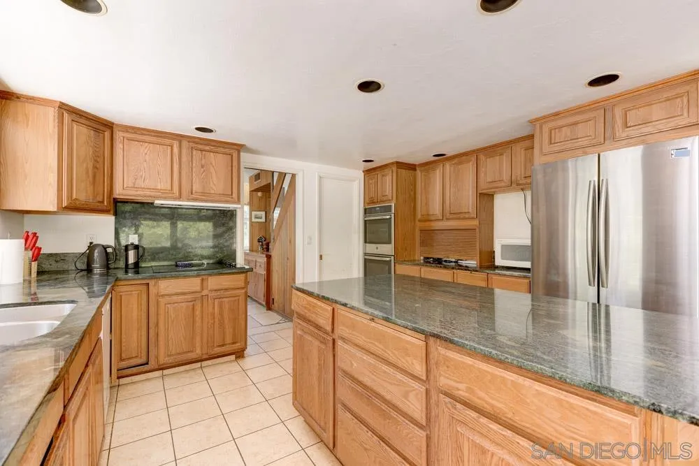 4954 Sun Valley Road Del Mar, CA 92014 - Photo 11 of 32 a kitchen with stainless steel appliances granite countertop a refrigerator a stove and white cabinets with wooden floor