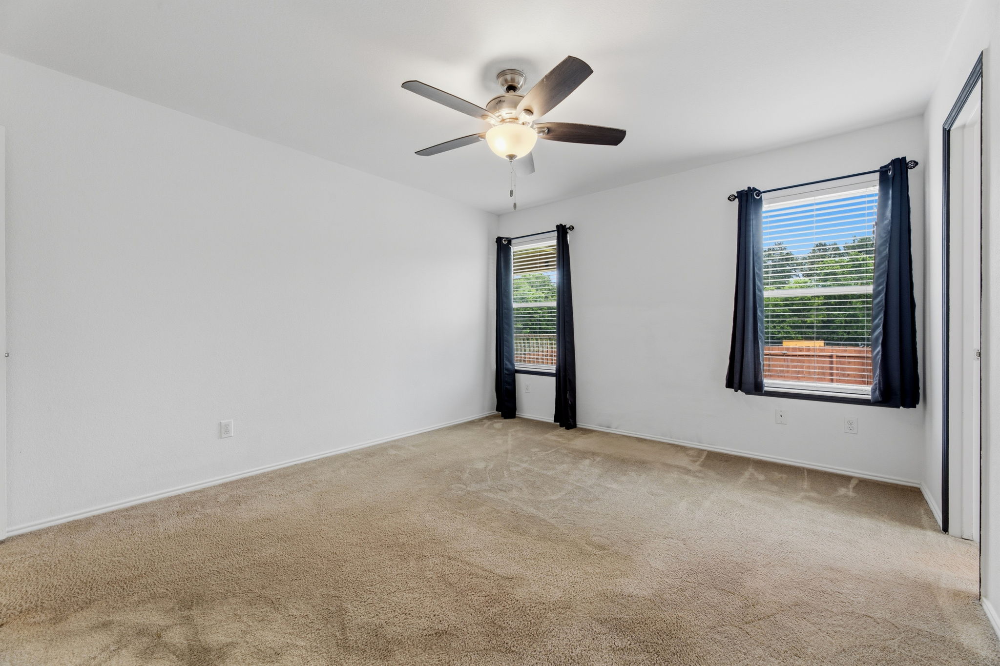 12601 Waynespur Lane Elgin, TX 78621 - Photo 28 of 38 A spacious bedroom with a neutral color palette, featuring a ceiling fan and two well-lit windows overlooking green surroundings.