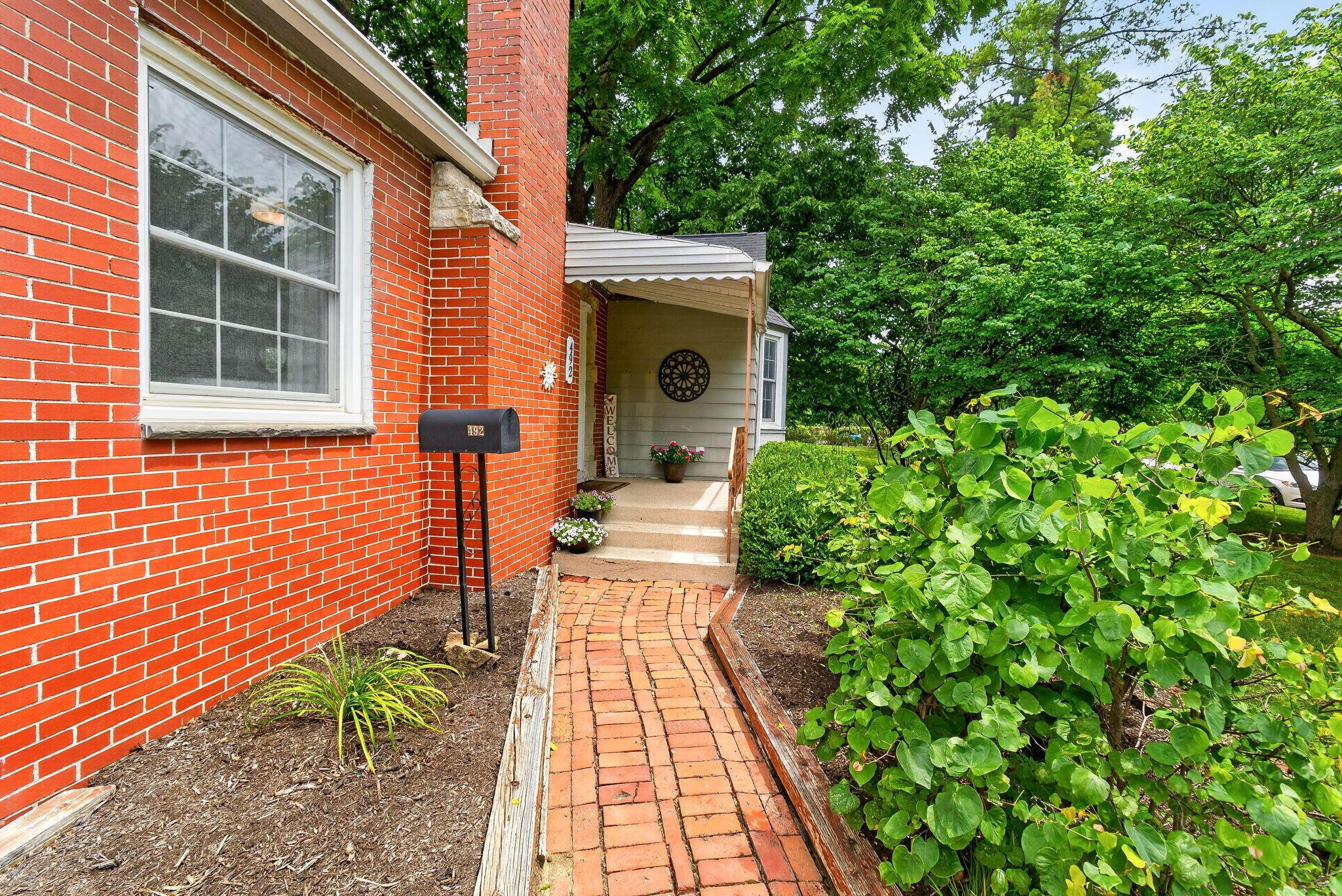 492 Wetmore Road Columbus, OH 43214 - Photo 11 of 55 Brick exterior featuring a white-trimmed window, a post-mounted mailbox, and a brick pathway leading to the covered porch entrance