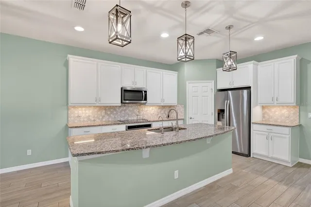 a kitchen with kitchen island stainless steel appliances granite countertop a sink a stove a refrigerator cabinets and chairs